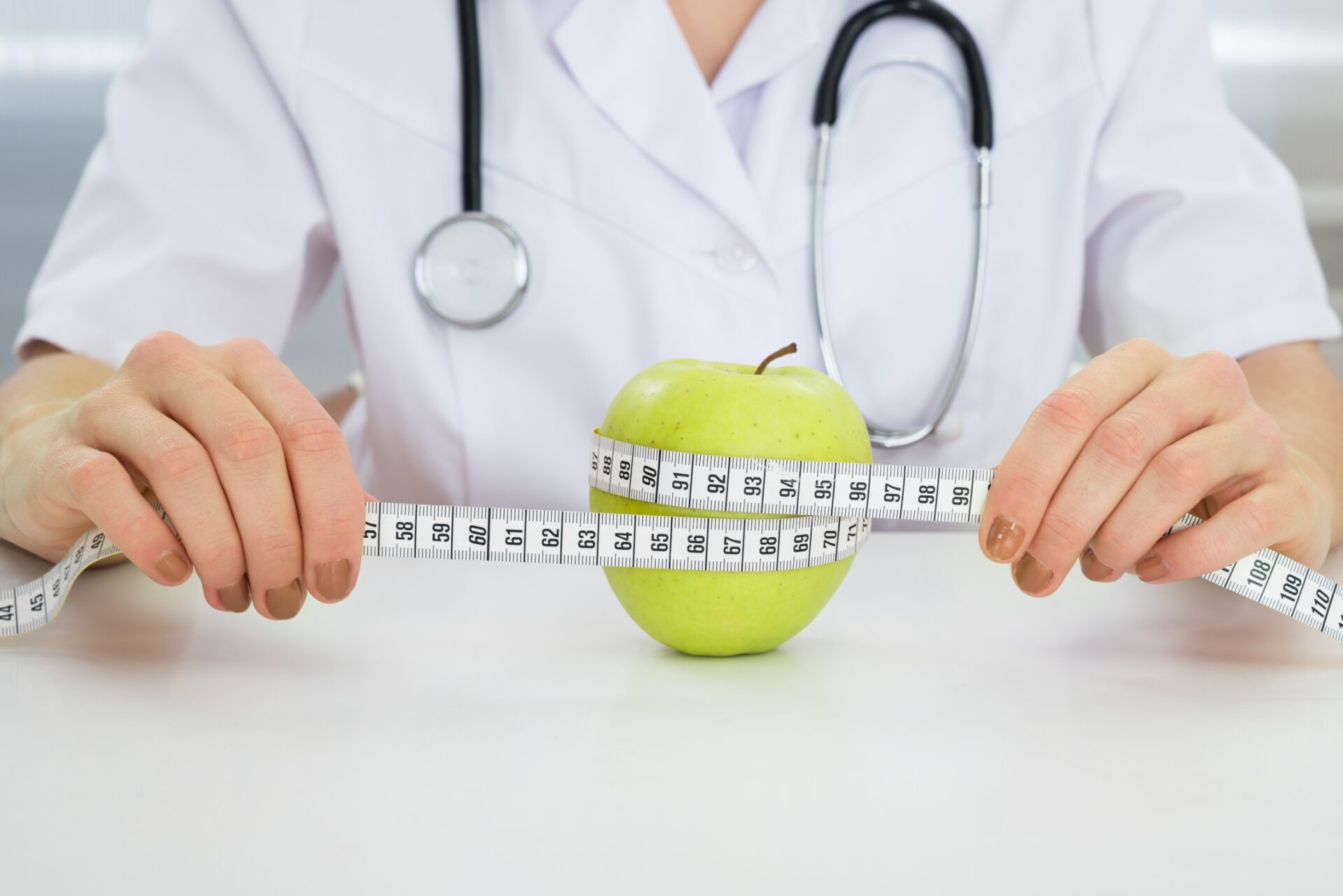 Close-up Of Dietician Measuring Green Apple With Measuring Tape