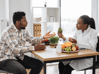 Handsome multiracial man in casual clothes visiting female dietitian in doctors office of medical center.