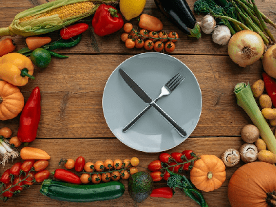 Knife and Fork on a Ceramic Plate Surrounded by Assorted Vegetables<br />
